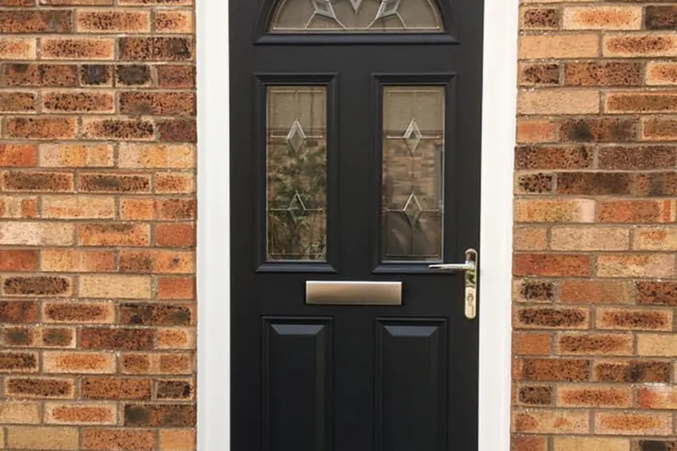 Black composite front door with decorative glazing in a brick porch